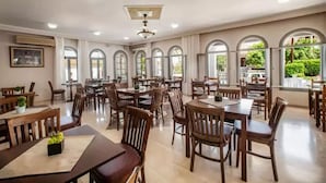 A spacious dining area with multiple tables and chairs, large windows with arched tops, and a ceiling fan.