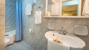 A bathroom with a bathtub, a sink, a mirror, and a toilet.