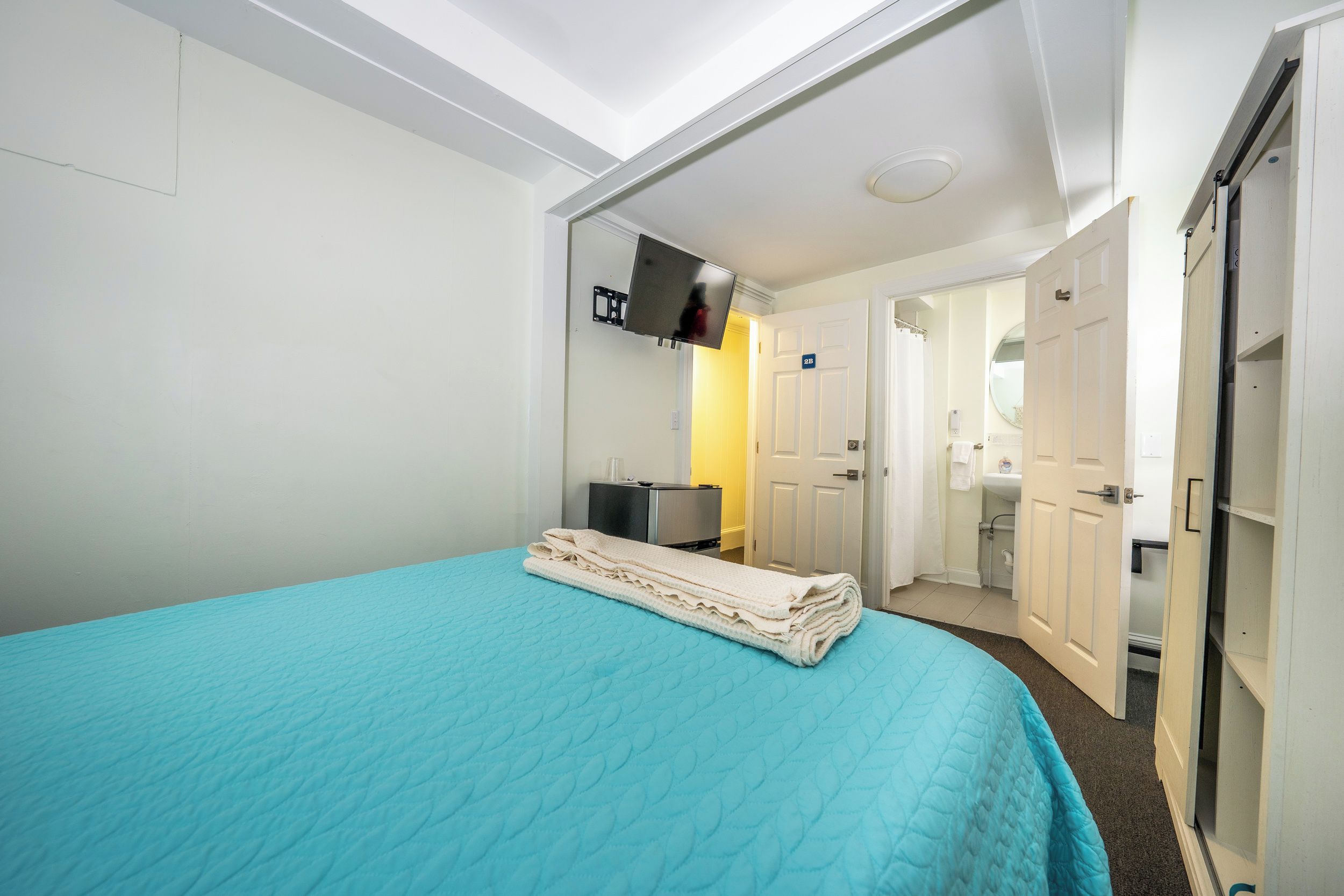 Een hotelkamer met een bed, een aan de muur bevestigde televisie, een badkamer door een open deur en een klein bureau met een stoel.