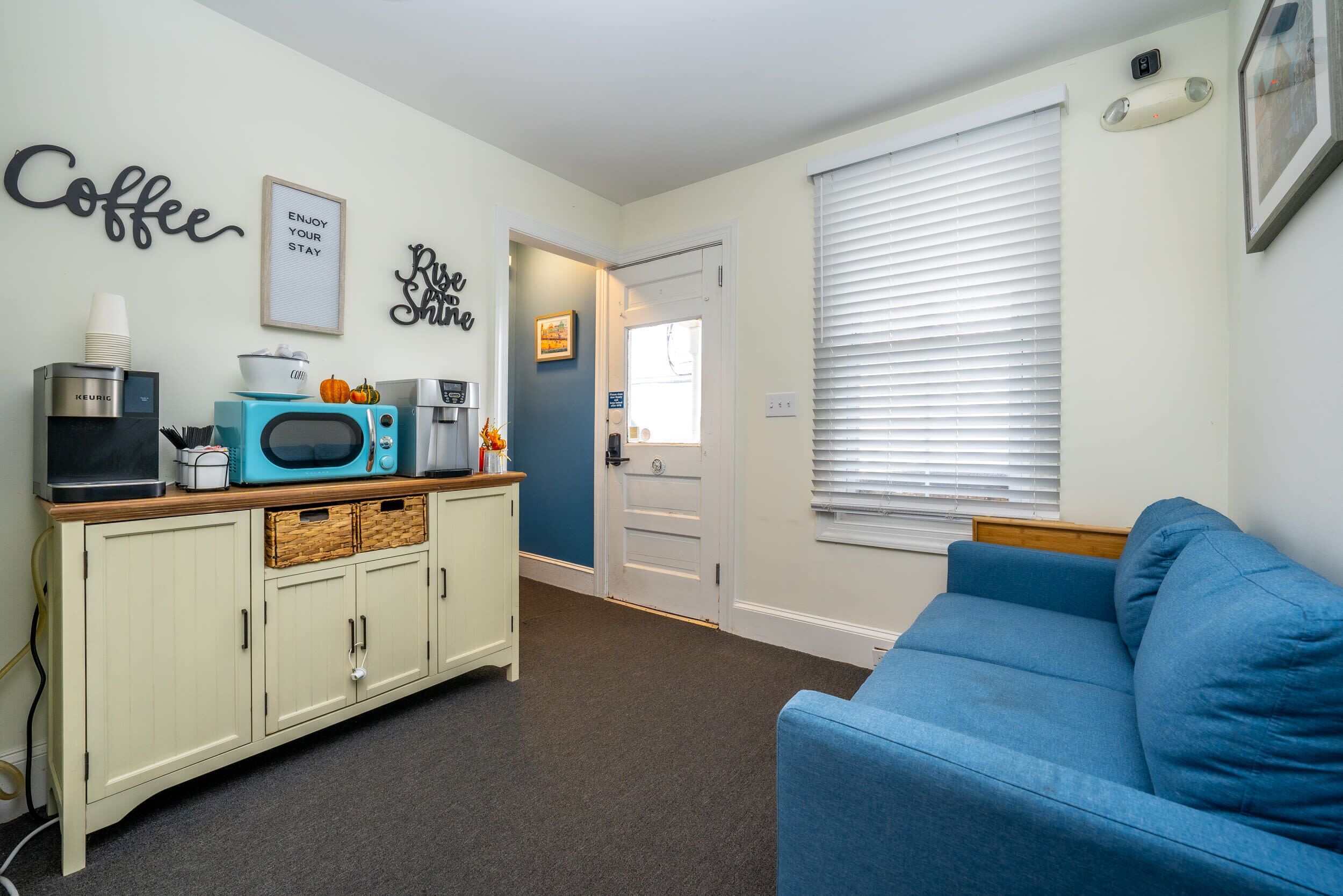 A compact living space with a kitchenette, a blue couch, and a door leading to another room.