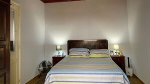 A bedroom with a wooden ceiling, a bed with striped bedding, two bedside tables with lamps, and a fan.