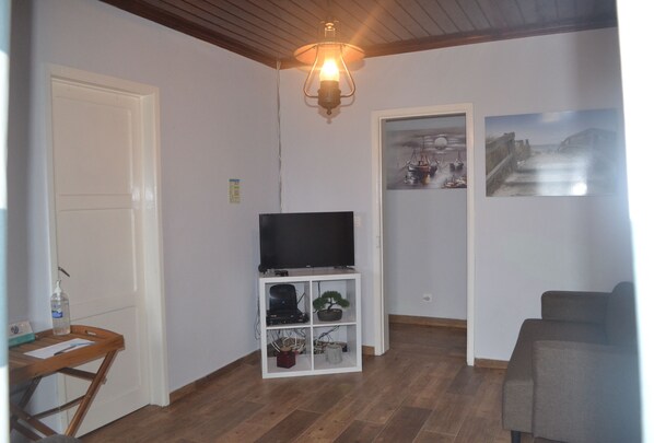 Un salon avec une télévision posée sur une étagère blanche, un canapé et deux tableaux encadrés accrochés au mur.