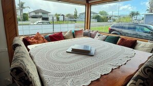 Een gezellig zitgedeelte met een houten tafel en een gehaakte tafelkleed, grote ramen met uitzicht op een woonstraat.