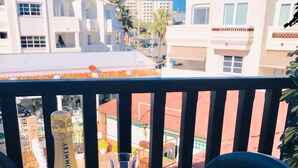 A table with a bottle of champagne, two glasses, and strawberries on a balcony overlooking buildings. - Apartamento Studio Marina Suite (Benalmádena)