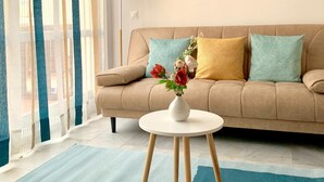 A modern living room with a beige sofa, a round mirror, and a vase with flowers on a small white table. - Apartamento Studio Marina Suite (Benalmádena)