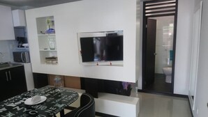 Ein gemütlicher Wohnbereich mit Esstisch, einem flachbildfernseher an der Wand, einer Küchenzeile mit Schränken und einem kleinen Badezimmer, das durch eine Tür erreichbar ist.