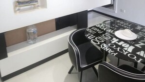 Ein moderner Essbereich mit einem schwarz-weißen Tisch, zwei Stühlen, einem Bücherregal und einer Vase, sowie einem Wand-Fernseher.