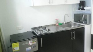 Eine kompakte Küche mit weißen Oberschränken, einem schwarzen Unterschrank, einer eingebauten Mikrowelle und einem kleinen Kühlschrank.