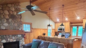 A cozy cabin interior with a stone fireplace, a wooden ceiling, a sofa, and a dining area. - Newfound Lake Bristol, NH Lakefront Cottage (Bristol)