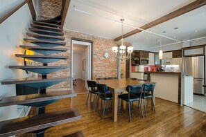 A modern kitchen with a brick wall, stainless steel appliances, and a wooden dining table with chairs. - Les Lofts St-Jo - By Les Lofts Vieux-Québec (Québec City)