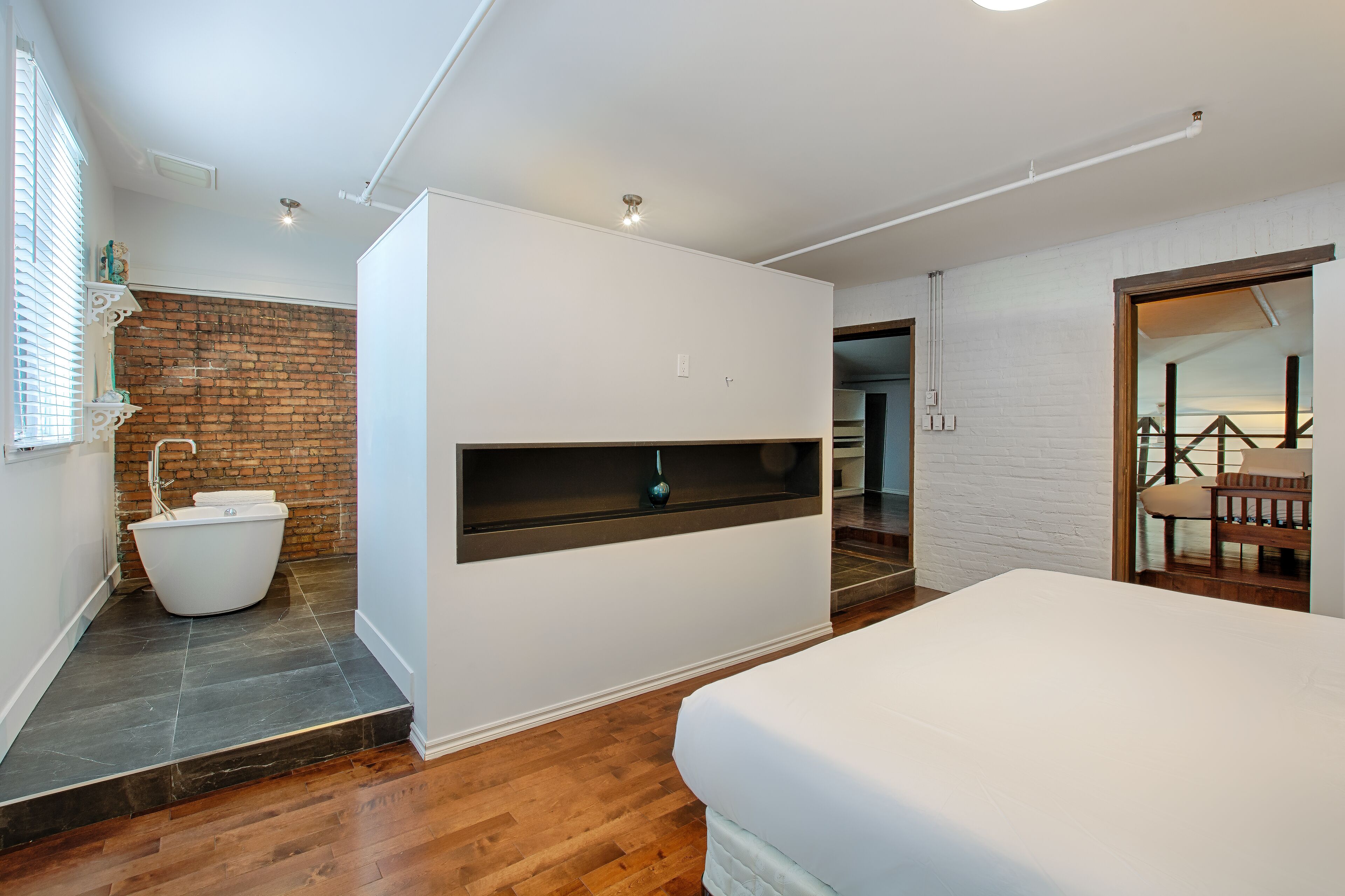 Een moderne slaapkamer met een groot bed, een inloopbad en een houten vloer.