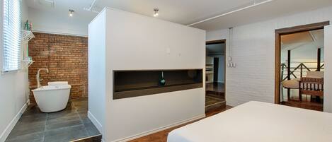 Een moderne slaapkamer met een groot bed, een inloopbad en een houten vloer.