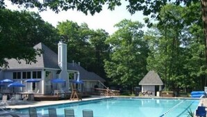 A swimming pool with lounge chairs and umbrellas, surrounded by trees and a house. - Cozy Mountain Retreat (Hidden Valley)