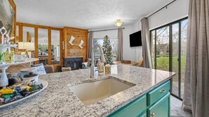 A modern kitchen with granite countertops, a sink, and a dining area with a Christmas tree. - Cozy Mountain Retreat (Hidden Valley)