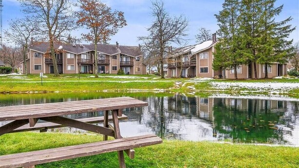 A residential building with a pond in the foreground, surrounded by trees and a picnic table. - Cozy Mountain Retreat (Hidden Valley)