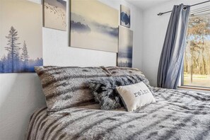 A bedroom with a bed, a pillow with 'relax' written on it, and wall art depicting nature scenes.