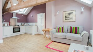 Un appartement moderne comprenant une cuisine, un espace de vie avec un canapé et des coussins colorés, une petite table et une lucarne.
