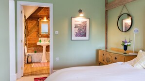 Une chambre à coucher comprenant un lit, une commode, un miroir, un tableau encadré, ainsi qu’une salle de bain avec un lavabo et un porte-serviettes.