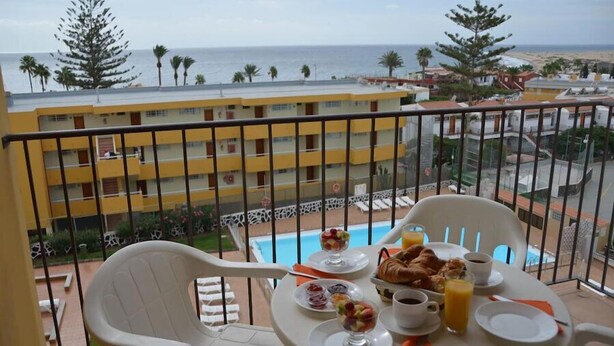 Un balcon avec une table préparée pour le petit-déjeuner, donnant sur une piscine et une plage.