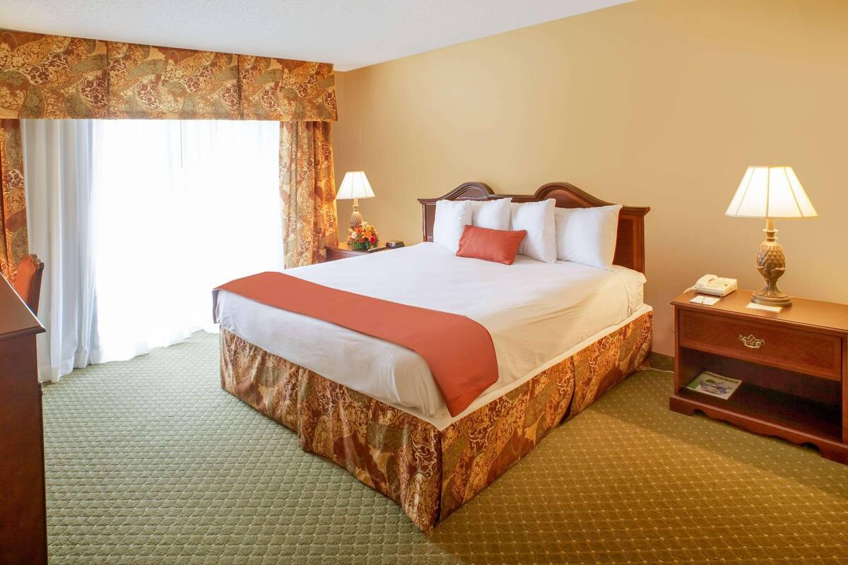 A hotel room with a large bed, two bedside tables with lamps, a curtain, and a carpeted floor.