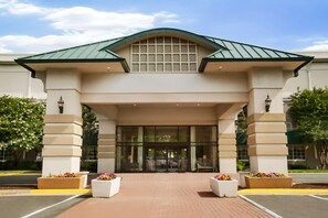 Entrada de hotel con un vestíbulo cubierto, puertas de vidrio amplias y jardines simétricos.