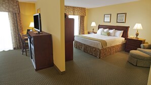 Una habitación de hotel con una cama, un escritorio con televisor, dos lámparas de noche, una silla y un aparador.