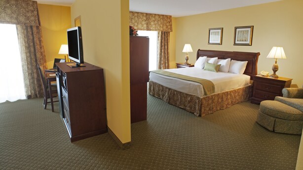 Une chambre d’hôtel comprenant un lit, un bureau avec une télévision, deux lampes de chevet, une chaise et une commode.