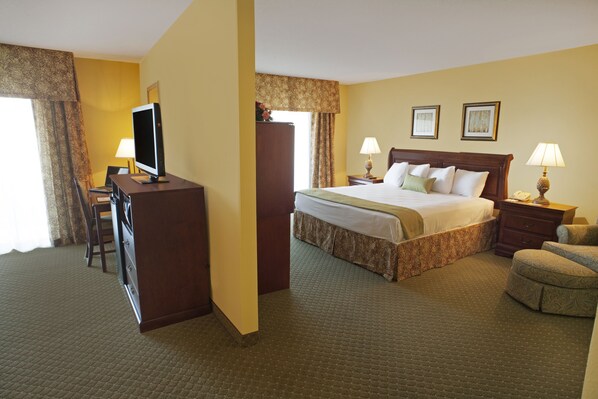 A hotel room with a bed, a desk with a television, two bedside lamps, a chair, and a dresser. - Clarion Suites Convention Center Fredericksburg (Fredericksburg)