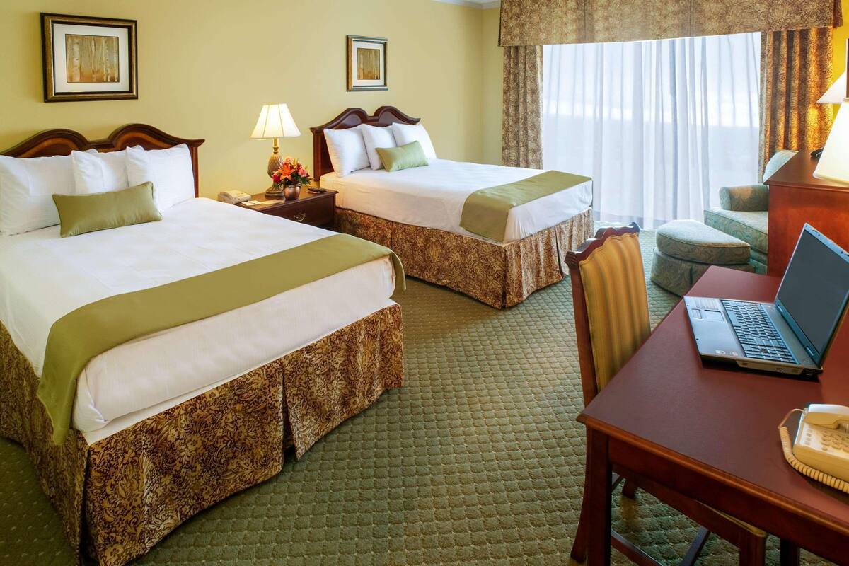 A hotel room with two beds, a desk with a laptop, a telephone, and a chair.
