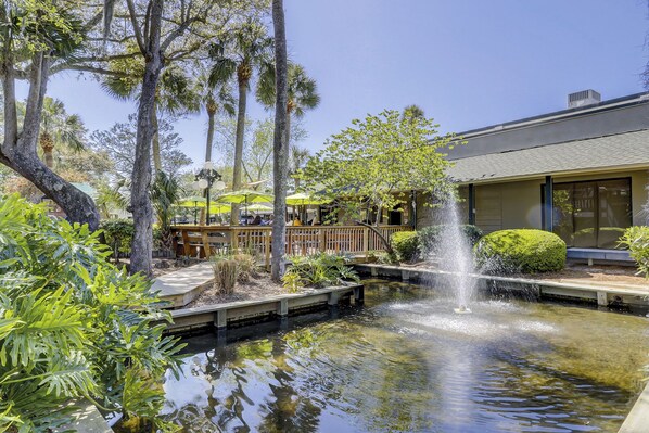 A tranquil outdoor area with a pond, a wooden deck, and a building with a covered seating area.
