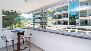 Un balcon avec une table et des chaises, de grandes fenêtres et une vue sur un immeuble moderne.