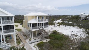 Ett hus vid kusten med en balkong, en terrass och en sandstrand i bakgrunden.