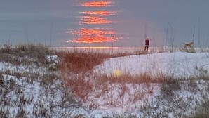 En solnedgång över ett vattenområde, med en person och en hund på stranden.