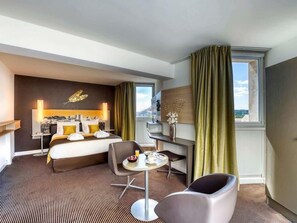 A hotel room with a bed, a desk, a chair, a small table with breakfast items, and a view of the outdoors. - Mercure Avignon Centre Palais des Papes Hotel (Avignon)