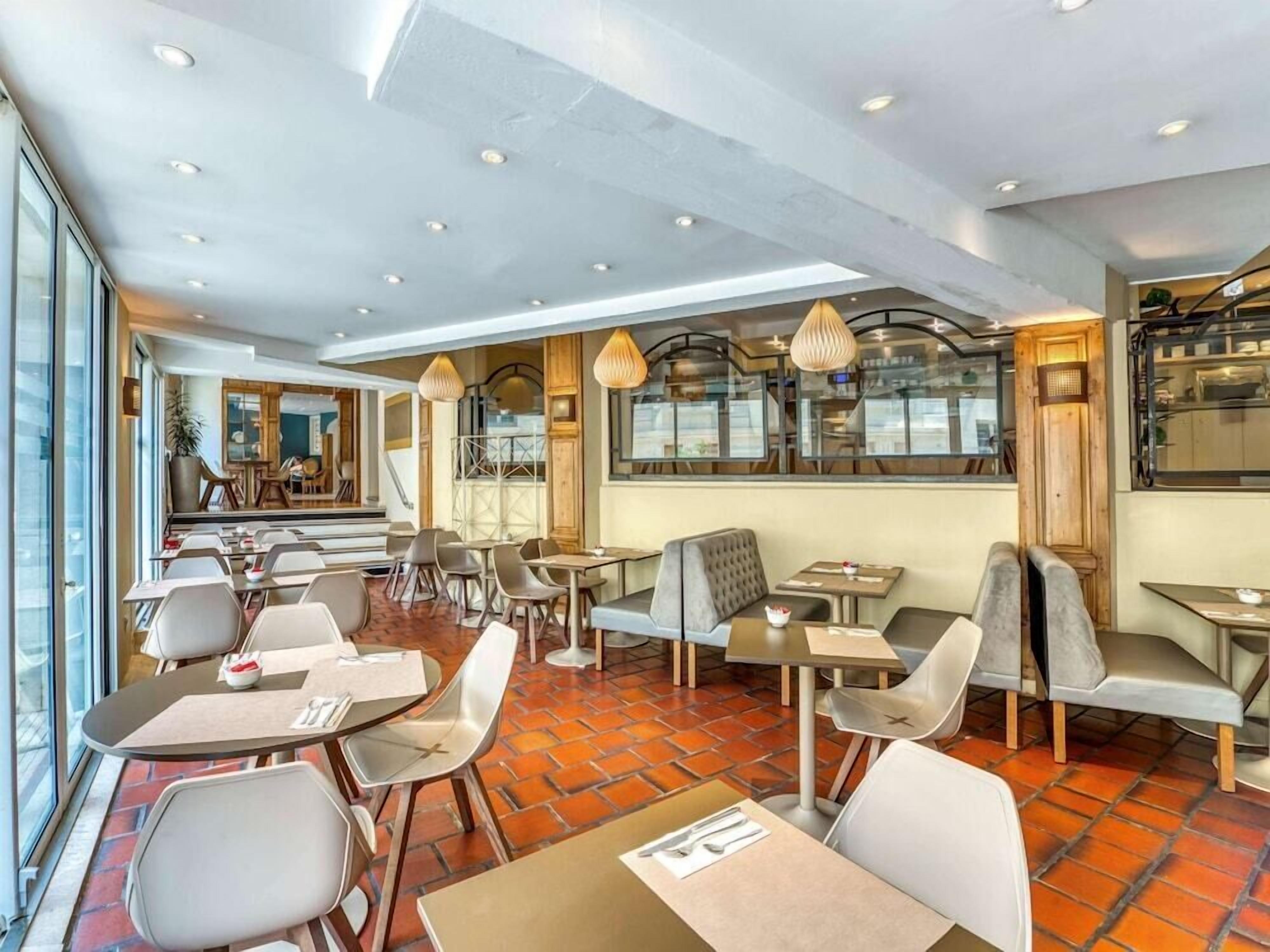 Un restaurante moderno con mesas y asientos tipo banca, piso de ladrillo y vista a la calle a través de grandes ventanales.