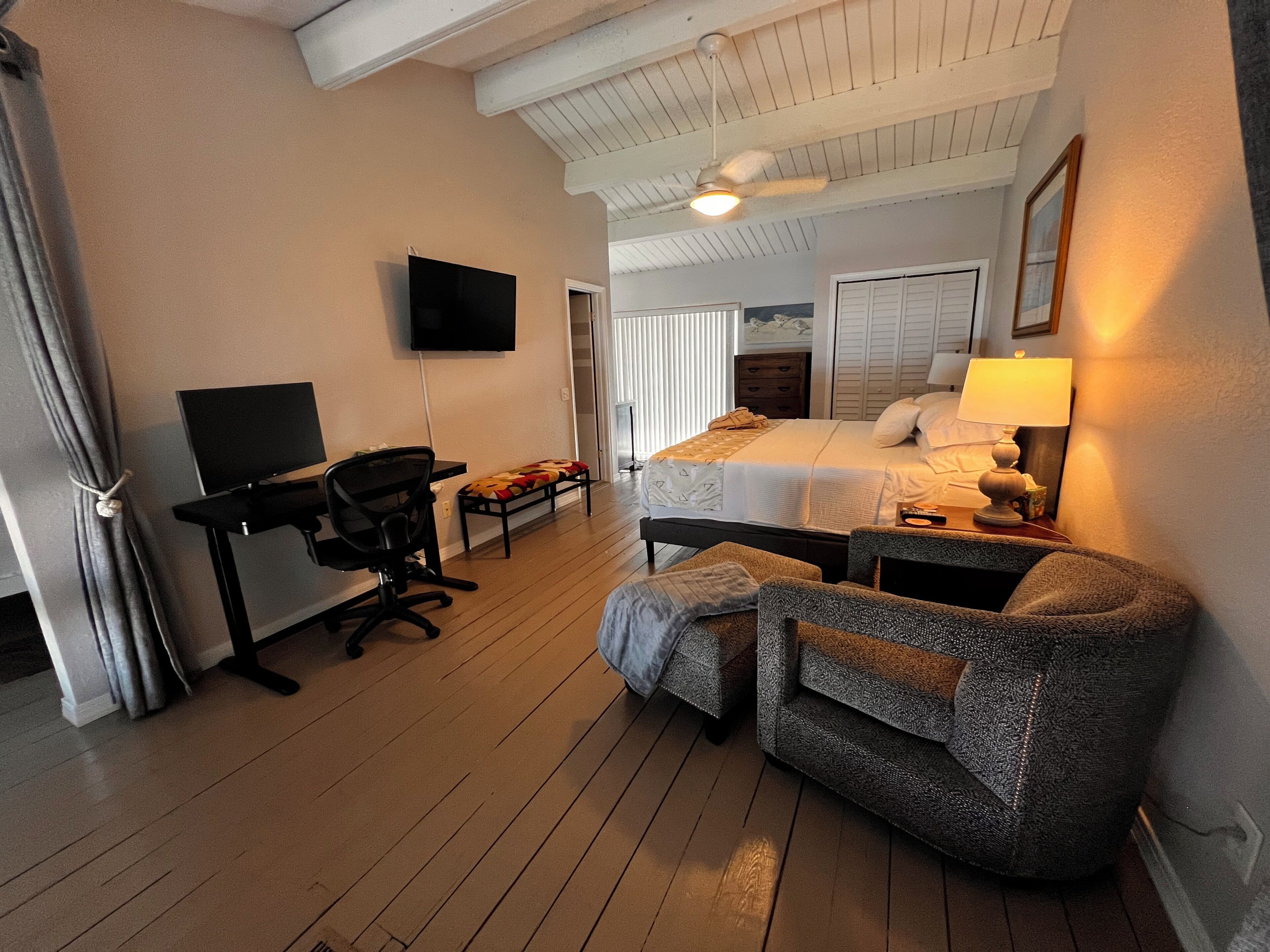 A hotel room with a bed, desk, chair, TV, and a ceiling fan.