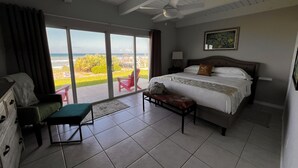 A bedroom with a bed, a bench, a nightstand, a ceiling fan, and a view of the beach.