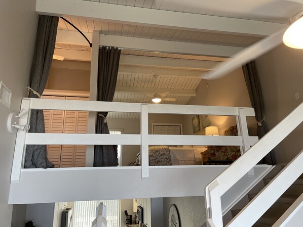 Una stanza con un letto a castello, una scala, una ventola a soffitto e una finestra con tende.