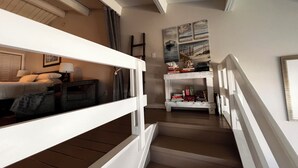 A staircase leading to a bedroom with a bed, a nightstand, and a lamp. There is a shelf with books and decorative items.