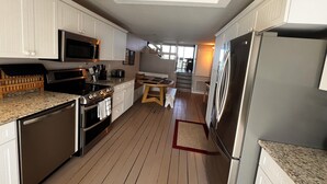 A kitchen with white cabinetry, stainless steel appliances, a wooden floor, and a view of the outdoors.