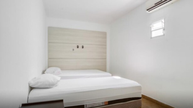Un dormitorio con cama, mesita de noche, aire acondicionado de pared y una ventana pequeña.