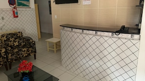 Zona de recepción con pared de azulejos, mostrador, teléfono, mapa enmarcado y un sofá.
