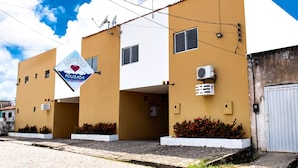 Un edificio de dos pisos con fachada amarilla, un cartel que dice 'Pousada' y un símbolo de corazón, y antenas parabólicas en el techo.