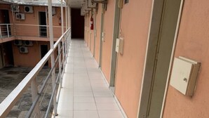 Un pasillo con suelo de baldosas, una barandilla metálica a un lado y una puerta al otro.