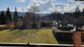A view of a grassy area with a white building, a wooden fence, and a mountain range in the background. - Ferienwohnung Bärenhofweg am Titisee (Titisee)