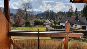 A wooden deck with a bamboo screen, overlooking a residential area with houses, trees, and a mountain range. - Ferienwohnung Bärenhofweg am Titisee (Titisee)