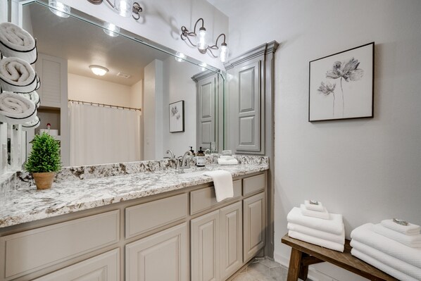 Un baño con encimera de mármol, un lavabo, un espejo, una planta en maceta y toallas sobre un banco.