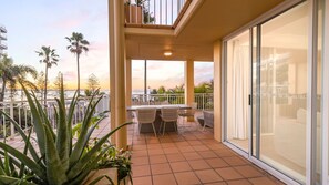 A balcony with a table and chairs, overlooking a body of water with palm trees.