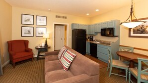A compact living space with a kitchenette, a sofa with a striped pillow, a red armchair, and a dining table with chairs. - 1 Bedroom Villa at Mountain Run at Boyne Mountain (Boyne Falls)
