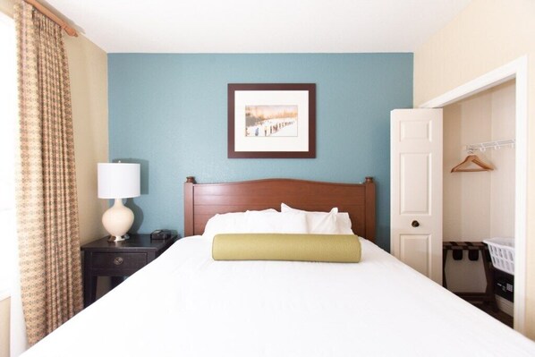 Habitación de hotel con cama, mesita de noche con lámpara, un cuadro en la pared y una puerta que da a un armario.